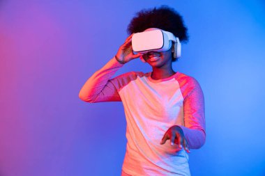 Genç Afrikalı, teknolojik dijital yenilik grafiğinde mavi neon aydınlatma grafiğinde izole edilmiş 3 boyutlu hologram veri uygulamasını seçmek için metaevren üzerinden VR gözlük takıyor. Entrika.