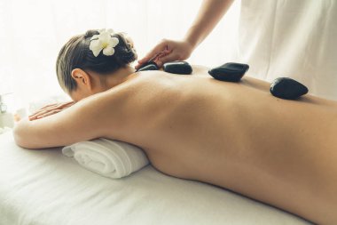 Lüks tatil köyündeki kaplıcalarda sıcak taş masajı. Gün ışığı sükunet ortamında, mutlu kadın müşteri bazalt taş masajından zevk alıyor. Rahatlatıcı bir sıcaklıkla vücudun üzerinde süzülüyor. Sessiz.