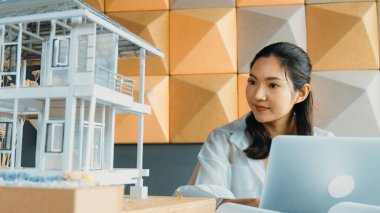 Genç ve güzel mimar mühendisin portresi çatı malzemelerini kontrol ediyor ve ofisteki masaya yerleştirilmiş proje planı ve ev modeliyle dizüstü bilgisayar kullanıyor. Yaratıcı iş tasarımı konsepti. Yönlendirici.