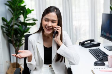 Gülümseyen güzel Asyalı iş kadını akıllı telefondan borsa grafiğini modern ofisteki bilgisayar ekranında analiz etmek için arıyor. Zenginliğe yüksek kazanç sağlama kavramı. Taktik.