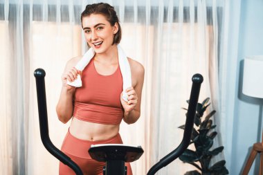 Spor ve atletik bir kadın, evdeki fiziğe ve sağlıklı spor yaşam tarzına uygun vücut egzersizi sırasında eliptik koşu makinesiyle koşuyor. Gaiety evde egzersiz eğitimi.