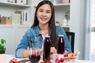 Gülümseyen, güzel Asyalı genç, lezzetli karışık çilek ve kiraz suyu detoksu içeceklerini inceleyen, sosyal medyada özel promosyon satışı için sağlıklı ürünler sergileyen. Taktik.