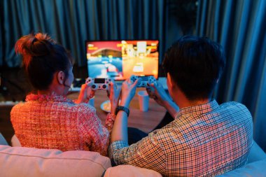 Kontrollü joystickli birkaç oyuncu, televizyon ekranında birlikte araba yarışı oyunu oynuyorlar. Arka tarafta atıştırmalıklar, modern konforlu evinde neon ışıklı oturma odasında kanepe. İnfobahn.