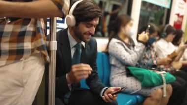 Gülümseyen yakışıklı yatırımcı trende otururken rahatlatıcı müzik dinliyor. Profesyonel iş adamı iş yerine toplu taşıma araçlarıyla giderken müzik dinlemeyi sever. Arka plan bulanık. Sevinçli..