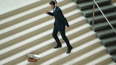 Kulaklıktan müzik eşliğinde merdivenlerde duran profesyonel bir iş adamı. Merdivenlere dizüstü bilgisayar yerleştirip dans ederken dinlenme sesi dinleyen yetenekli bir proje yöneticisi. Modern dans. Sevinçli..