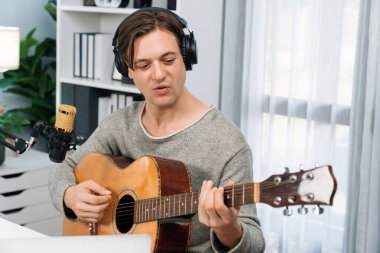 Gülümseyen yüzlü akıllı şarkıcının sunucu kanalı, şarkı söylerken gitar çalmak, sosyal medya kanalında yayın yapmak, modern stüdyo kaydında video kaydedici olarak kulaklık takmak. Bireysel.