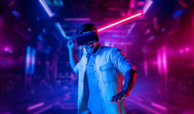 Lazer kılıcı tutan ve VR gözlük takan oyuncu. Beyaz adam, neon şatonun etrafında dikilirken görsel gerçeklik kulaklığı kullanıyor. Yenilik teknolojisi. Sapma.