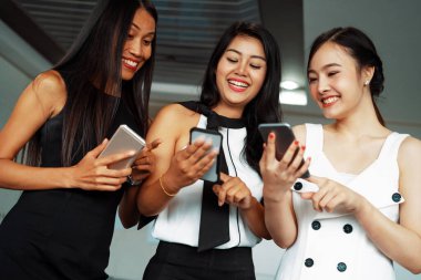 Üç kadın arkadaş ellerinde cep telefonuyla sohbet ediyorlar. Sosyal medya, dedikodu haberleri ve online alışveriş kavramı. uds