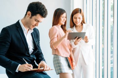 Kitap okuyan ve iş yerinde iş arkadaşları ve arkadaşlarıyla çalışan genç ve yakışıklı bir işadamı. Kurumsal iş adamları grubu. uds