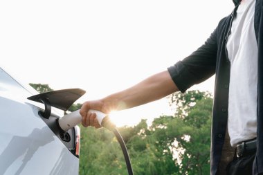 Yolculuk sırasında doğal ormanlarda ya da güneş ışığı alan ulusal parklarda elektrikli araba için şarj olan bir adam. Tatil ve tatil boyunca çevre dostu seyahat. Yükselt