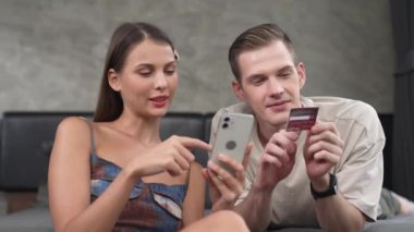Genç çift, kredi kartıyla ödemek için internet üzerinden ödeme uygulaması ve dijital cüzdan kullanarak yatak odasında oturuyor. Mobil internet üzerinden alışveriş ve modern alımlar. Düzenle
