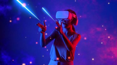 Heyecanlı, gülümseyen bir kadın VR 'ı açarken metaevren transferi yapıyor. 3D hologram oyun alanı savaşında, ışık saçan Bokeh galaksisi siberalayı ile birlikte el yapımı mermi tabancası lazeri kullanıyor. Halüsinasyon.