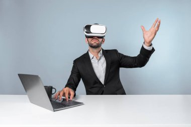 Bilgisayarla masada otururken ve VR gözlüğü takarken veri analizine bakan yetenekli bir iş adamı. Proje yöneticisi sanal gerçeklik sistemini kullanarak ya da metaevrende bağlantı kurarak çalışıyor. Sapma.