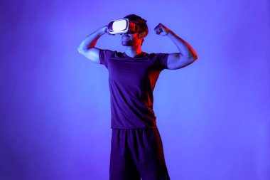 Sanal gerçeklik gözlüklü mutlu bir adam neon ışıklı arka planda kaslarını esnetiyor. Sıradan kıyafet giyen, sanal gerçeklik simülatörü teknolojisi kullanarak rahatlayan ve egzersiz yapan sağlıklı bir insan. Sağlıklı temsil et. Sapma.