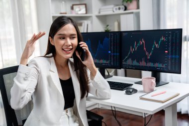 Genç ve güzel Asyalı iş kadını, modern ofisteki bilgisayar ekranlarında her borsa grafiğinde kârlı bir hisse senedi grafiğiyle istikrarlı veya daha yüksek kar değerini analiz etmek için komisyoncuyu telefonla arıyor. Taktik.