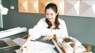 Mimari model, dizüstü bilgisayar ve planla not alırken kalem kullanarak ev modelini ölçen genç ve güzel mimar mühendisinin portresi. Yaratıcı iş tasarımı konsepti. Yönlendirici.