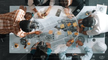 Profesyonel inşaat mühendisi ekibinin üst düzey görüşü ev modeline yapışkan notlar yazıp not tutarken iç mimar da finansal istatistik tablosunu tartışıyor. Hizalama.