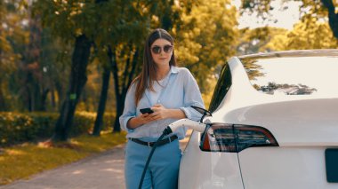 Ulusal Park veya Yaz Ormanı 'ndaki tatil gezisi sırasında EV şarj istasyonundan elektrik aküsü almak için akıllı telefon internet bankacılığı başvurusu yapan bir kadın. Yükselt