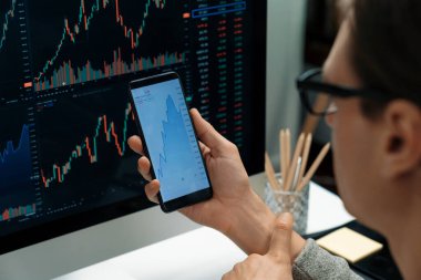 Akıllı borsa yatırımcıları ekranda akıllı telefon ile piyasa borsasını işaret ederek dizüstü bilgisayarın yanı sıra en yüksek dinamik yatırım oranını göstererek, modern işyerindeki veri planlamasına odaklanıyorlar. Bireysel.