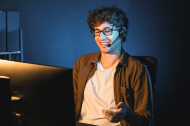 Genç yaratıcı iş adamı, bilgisayar ekranında dinleyicilerle iletişim kuruyor ya da takım üyesiyle görüşüyor. Neon Light Modern Ev Ofisi 'nde kulaklık takıyor. Gece vakti çalışma kavramı. Toplayıcı.