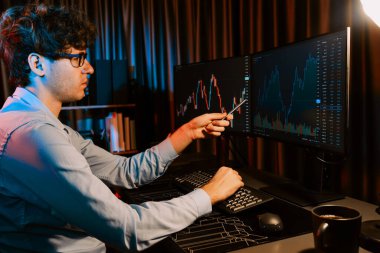 Genç yatırımcı hisse senedi tüccarı internetteki mevcut pazar grafiğinin çekici dinamik döviz kuru ekranlarıyla karşılaştırarak modern ofisteki finans grafik monitörünü işaret ediyor. Toplayıcı.