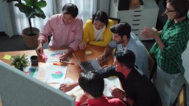 Çeşitli insanlardan oluşan bir grup, el çırparken yapışkan bir notla pazarlama planı yapıyor. Top view dizüstü bilgisayarla çalışırken borsa yatırımını tartışıyor ve konuşuyor. Cemaat.