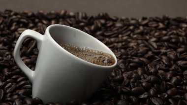 Kahve fincanının içine kahve çekirdeği yığını ile çevrili bir şekilde düşüyor. Beyaz fincana aromatik fasulye döküyorum. Kahvenin üst görüntüsü siyah arka planlı cama düşer. Geliştirilebilir.