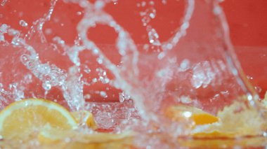 Kırmızı zemine serpiştirilmiş taze limon dilimlerini kapatın. Dilimlenmiş limon düşüşü ve suya düşme makrosu. Tazelik ve susuzluk kavramı. Citrus. Poster için tasarım. Pabulum.