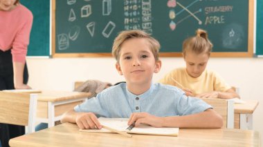 Çekici beyaz çocuk okulda matematik okurken kameraya bakıyor. Çeşitli şirin öğrenciler test yaparken öğretmen Asyalı çocuklara soru sorup tahtaya kağıt doğrultuyor. Pedagoji.