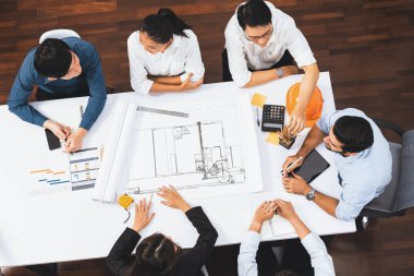 Mimari proje üzerinde birlikte çalışan, inşaat planını gözden geçiren ve toplantı masasında plan oluşturan çeşitli inşaat mühendisi ve müşteri gruplarından oluşan üst düzey bir pankart. Tedbirli