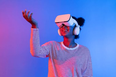 VR kullanan gülümseyen Afrikalı kadın meta-evren çiçekleri aracılığıyla güzel kokuyor ve kelebek böceği hologramı canlı pembe ışıklı arka plan teknolojisi 3D siber uzay. Entrika.