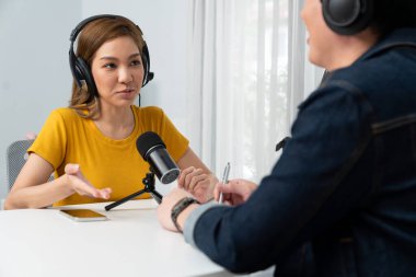 Gülümseyen radyo etkili sunucusu kulaklık takıyor kadın konuşmacı ile röportaj yapıyor sosyal medya internet sitesinden dinleyicilere bilgi paylaşıyor stüdyo kaydında sabah canlı yayın kanalı. İnfobahn.