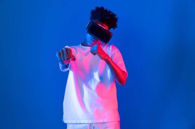 VR giyen Afro-Amerikan boksör boksör boksör, boksör yumruğu kamerasıyla fütüristik teknoloji sanal gerçeklik metaevren dövüş kutusunu birbirine bağlayan izole edilmiş pembe ışıklı duvar pozu veriyor. Entrika.