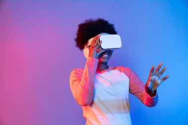 Genç Afrikalı, teknolojik dijital yenilik grafiğinde mavi neon aydınlatma grafiğinde izole edilmiş 3 boyutlu hologram veri uygulamasını seçmek için metaevren üzerinden VR gözlük takıyor. Entrika.