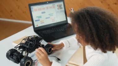 Akıllı Afrikalı kız dizüstü bilgisayar mühendisliği ödevi yaparken araba modelini tamir etmek ya da yapmak için tornavida kullanıyor. Çocuk kodlama ve programlama sistemi yazarken robotik araba üzerinde çalışıyor. Etkinlik.