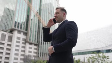 Yetenekli bir iş adamı pazarlama ekibiyle pazarlama stratejisi hakkında konuşurken gökdelende dururken telefon kullanıyor. Mutlu yönetici, modern kentsel şehirdeki satışları arttırmak için meslektaşını arıyor. Urbane.