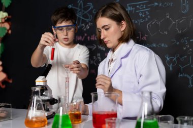 Öğretmen, laboratuarda öğrenciyi destekliyor. Öğrenci ve öğretmen cam kapta sıvı kullanarak STEM sınıfında kimya bilimi üzerine deney yapıyorlar. Karıştırma çözeltisi. Etkinlik.