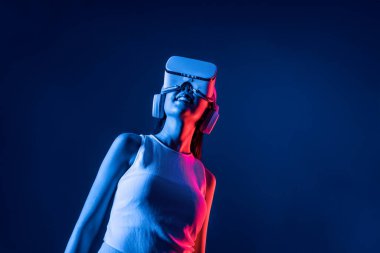 Siberpunk neon ışıklı cihazlarla çevrili zeki bir kadın metaevrene bağlı VR kulaklık takıyor, gelecekçi siber uzay teknolojisi. Zarif bir kadın sanal ortamda yaratılmış gibi görünür. Halüsinasyon.