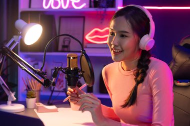 Geceleri podcast 'te olumlu konuşmalar yapan, pembe neon ışıklı modern stüdyoda sunum için dizüstü bilgisayar kullanan, gülümseyen, genç, güzel Asyalı bir etkileyiciydi. Taktik.