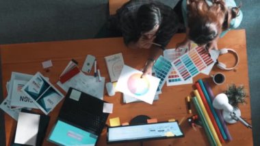 Akıllı tasarımcının renkli paletlerden renk seçmesine yardım ederken yukarıdan aşağı görünümü. Dizüstü bilgisayardan logoya bakarken birlikte çalışan ve planlayan iş adamlarının hava görüntüsü. Sempozyum.