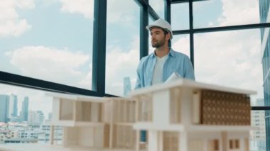 Gökdelen manzarasına bakarken yürüyen profesyonel mimar mühendisi. Masaya yerleştirilmiş ev modeliyle pencereye bakarken yetenekli proje yöneticisi proje planını tutuyor. Tasarım. İzleme