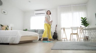 Modern apartman dairesinde dans ederken yerleri paspaslayan beyaz bir hizmetçi. Mutlu enerjik anne ya da temizlikçi müzik eşliğinde oturma odasını temizlemekten zevk alır. Yaşam tarzı. Pedagoji.