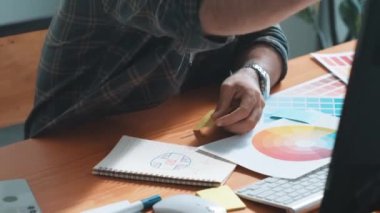 Toplantıda profesyonel tasarımcı yazma ve logo grafiği tasarlama. Renkli paletler üzerinde çalışan iş adamlarının yakınlaşması ve masaya kağıt ve ekipman ile yapışkan notlar yazmak. Sempozyum.