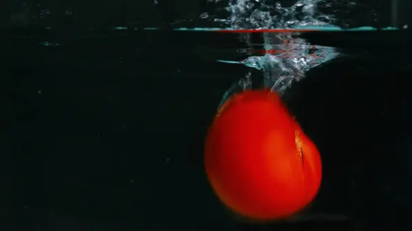 Stock image A close up of a fresh vibrant red tomato floating in clear water with black background. Macrography of organic apple falling and dropping in to splashing cool water. Freshness concept. Pabulum.