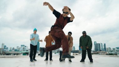 Profesyonel Asyalı sokak dansçısı çatıda çok kültürlü arkadaşlar dans ederken B boy dansı yapıyor. Genç modern dans grubu hip hop hareketi yapıyor. Tarz, moda, aksiyon. Açık hava sporu 2024. Hiphop.