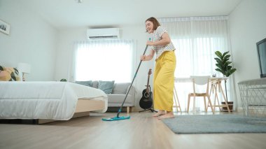 Modern apartman dairesinde dans ederken yerleri paspaslayan beyaz bir hizmetçi. Mutlu enerjik anne ya da temizlikçi müzik eşliğinde oturma odasını temizlemekten zevk alır. Yaşam tarzı. Pedagoji.