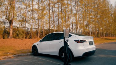 EV elektrikli araç EV şarj istasyonu ulusal park veya açık hava orman manzaralı. Sonbahar mevsimi ormanlarında çevre dostu EV arabalarla doğal koruma. Yükselt