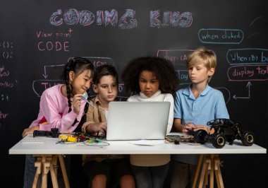 STEM sınıfında sınıf öğrencisi robot araba kodlamayı öğreniyor. Çocuklar dizüstü bilgisayara bakıp düşünüyor. Erkek ve kız ciddi görünüyor, ama pembe elbiseli tek çocuk komik görünüyor. Etkinlik.