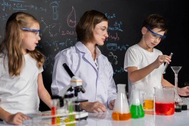 Laboratuvarda çalışan öğretmen, güvenlik gözlüğü takıyor, STEM sınıfında kimya bilimi üzerine deney yapıyor. Öğrenci komedisi tüpte sıvı deneyi yapar. Etkinlik.