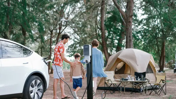 stock image Outdoor adventure and family vacation camping in nature travel by eco friendly car for sustainable future. Lovely family recharge EV car with EV charging station in campsite. Perpetual